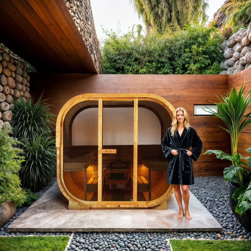 Woman in a black robe standing in front of a modern wooden sauna with plants around.
