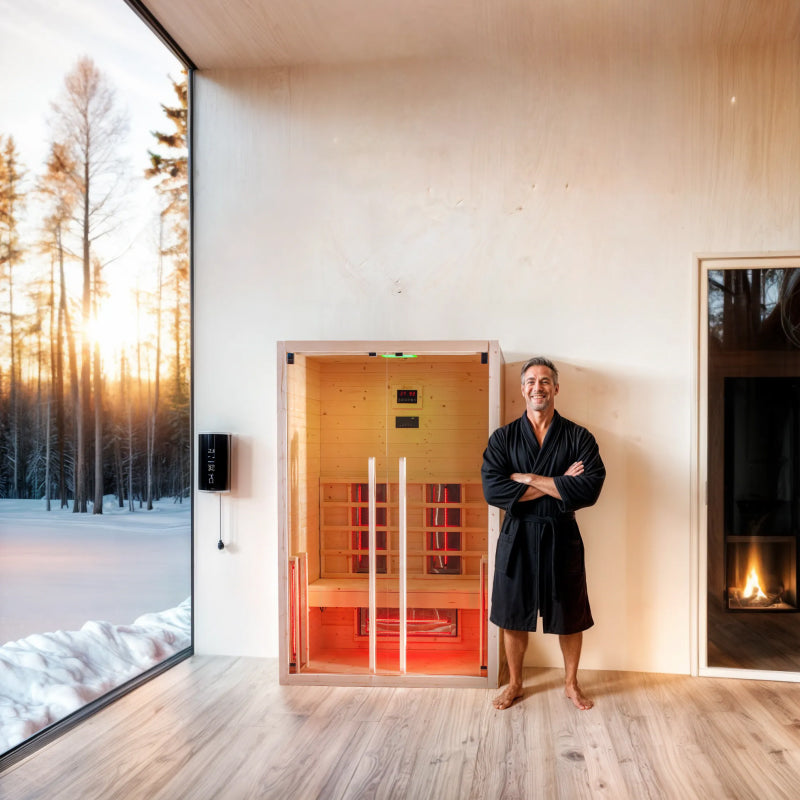 Man in a black robe standing in a modern room with a Dharani S2 infrared sauna and fireplace.
